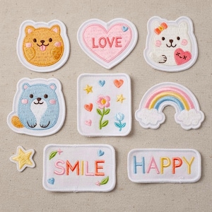 Puede incluir: Una colección de parches bordados en varias formas y diseños. Incluye un oso, un corazón con "LOVE", un oso con un lazo, un oso azul, un cuadrado con una flor, un arcoíris, una estrella y parches con "SMILE" y "HAPPY".