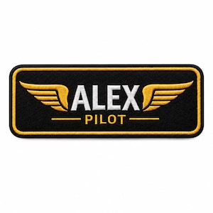 Op de afbeelding: Een rechthoekige geborduurde patch met een zwarte achtergrond en een gouden rand. De tekst ALEX is in het wit, gecentreerd tussen twee gouden vleugels. Daaronder staat het woord PILOT in goud, geflankeerd door twee gouden lijnen op zwart.
