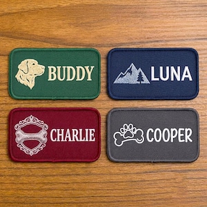Op de afbeelding: Vier rechthoekige geborduurde patches met afgeronde hoeken. De groene patch toont een hondenkop en de naam BUDDY. De blauwe patch toont een berg en de naam LUNA. De rode patch toont een bot in een kader en CHARLIE. De grijze patch toont een pootafdruk op een bot en COOPER.