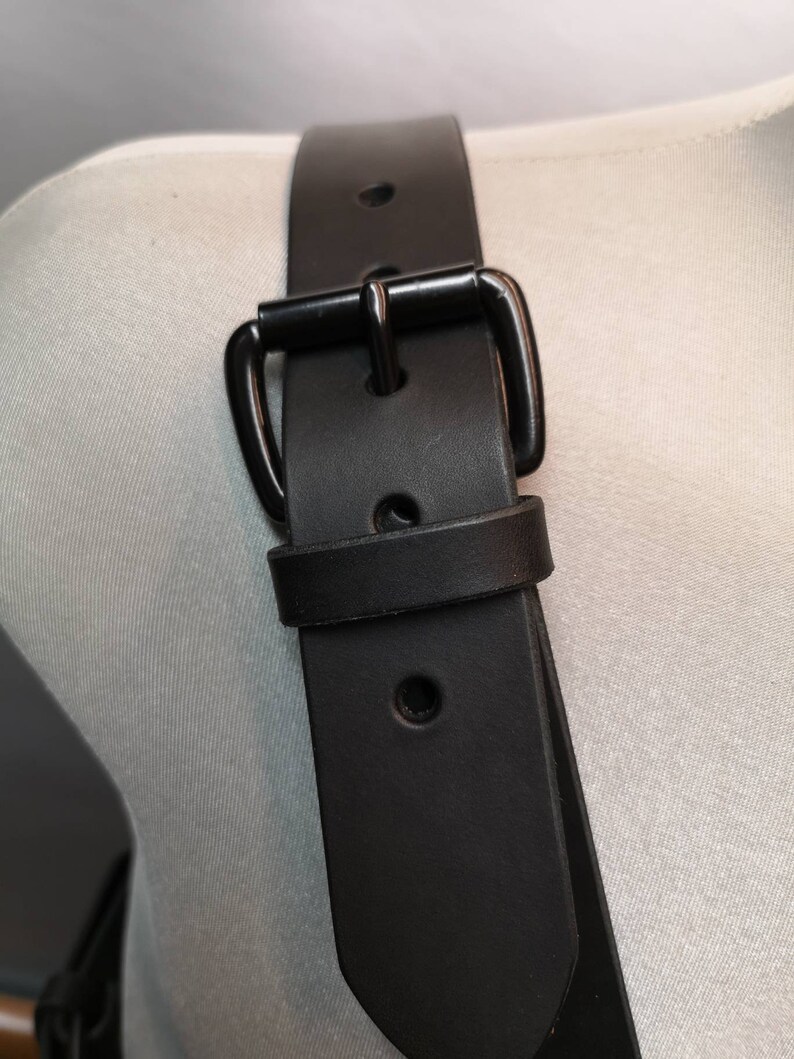 Op de afbeelding: Zwarte leren riem met een zwarte metalen gesp. De riem wordt getoond op een wit mannequin.