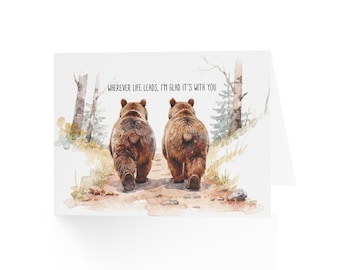 May include: A greeting card featuring a watercolour illustration of two brown bears walking away on a dirt path through a forest. The text above the bears reads, "WHEREVER LIFE LEADS, I'M GLAD IT'S WITH YOU." The scene includes trees and foliage.
