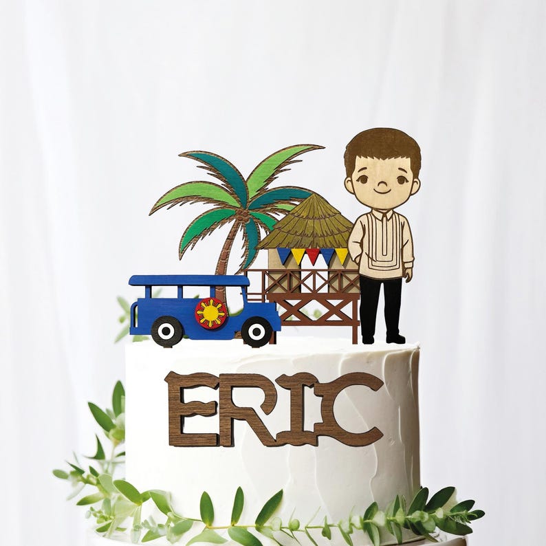 May include: A cake topper featuring a blue jeepney with a sun emblem, a palm tree, a hut, and a cartoon figure. The name "ERIC" is displayed in wooden letters on the cake.