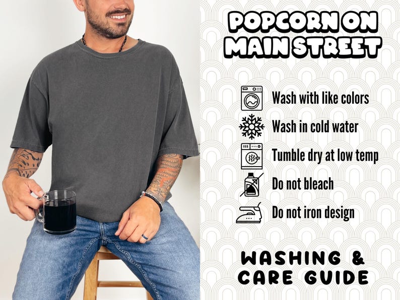 Puede incluir: Una camiseta gris oscuro con el texto "Popcorn on Main Street" impreso en ella. La imagen tambi&eacute;n incluye una gu&iacute;a de lavado y cuidado con instrucciones para lavar con colores similares, lavar con agua fr&iacute;a, secar en secadora a baja temperatura, no usar lej&iacute;a y no planchar el dise&ntilde;o.