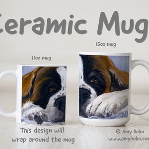 May include: Two white ceramic mugs with a brown and white dog illustration. The 11oz mug shows the dog's face and the 15oz mug shows the dog's face and paw. The text "This design will wrap around the mug" is below the smaller mug. The text "Amy Bolin www.amybolin.com" is below the larger mug.