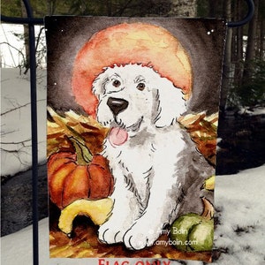May include: A white dog with a black nose and tongue sits in front of a large orange pumpkin. The dog is sitting in a pile of brown leaves. The background is a dark blue sky with a large orange moon.