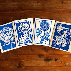 May include: Four floral art prints with blue and white designs. Each print features a different flower, including a peony, poppy, and lily. The prints are displayed on a wooden surface.