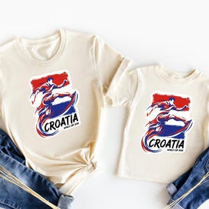 two white t-shirts with the word "Crotia" printed on them, along with a graphic of a person riding a skateboard. The t-shirts are laid out on a white background, with a pair of blue jeans visible in the foreground.