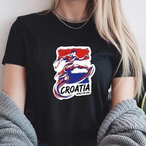 A person wearing a black t-shirt with a graphic design featuring a figure in a red, white, and blue outfit, along with the text "Croatia" and "World Cup of Croatia".