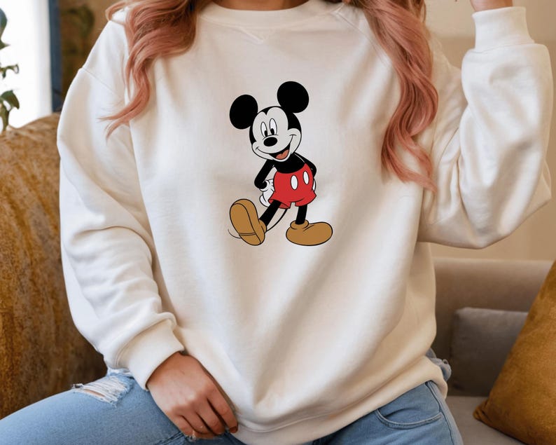 A person wearing a white sweatshirt with a Mickey Mouse graphic printed on it.