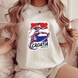 A woman wearing a white t-shirt with a graphic of a person surfing and the text "Crotia World Cup 2018" printed on it.
