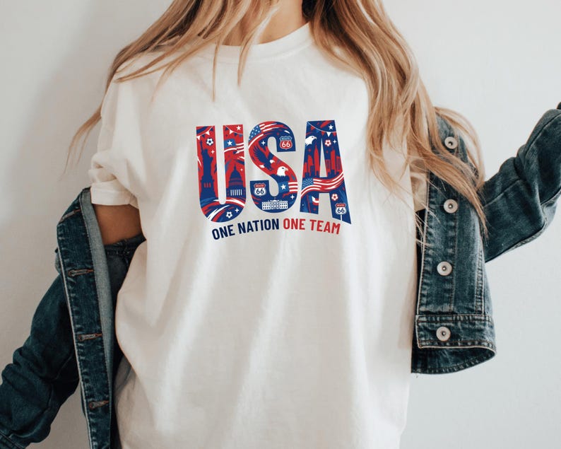A person wearing a white t-shirt with the text "USA" and "ONE NATION ONE TEAM" printed on it, along with various patriotic symbols.