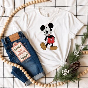 a white t-shirt with a Mickey Mouse graphic, a pair of blue jeans, and some Christmas decorations, including a string of beads and pine cones.