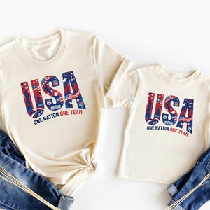 two white t-shirts with the text "USA" printed on them, along with a pair of blue jeans.