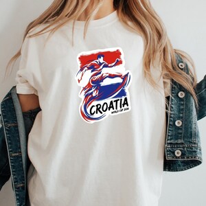A person wearing a white t-shirt with a graphic design of a person in a fighting stance and the text "Croatia" printed on it.