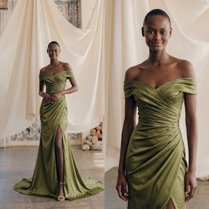 Könnte beinhalten: Ein olivgrünes schulterfreies Kleid mit einem hohen Schlitz. Das Kleid hat ein drapiertes Oberteil und einen fließenden Rock. Das Model trägt das Kleid in einem Studio mit weichem, neutralfarbenem Stoff im Hintergrund.