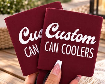 May include: Two burgundy foam can coolers featuring the white text Custom CAN COOLERS printed on the front. The sleeves are made of a soft, flexible material designed to insulate beverage cans, with a flat, rectangular shape and open top.