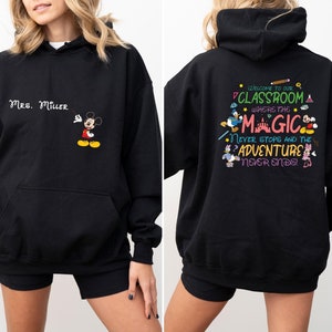 May include: Black hooded sweatshirt with a Mickey Mouse design on the front and a Disney-themed classroom quote on the back. The quote reads "Welcome to our classroom where the magic never stops and the adventure never ends!"