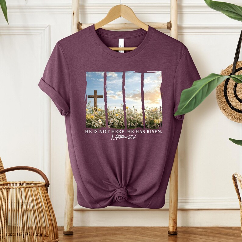 May include: A maroon t-shirt with a graphic of a cross in a field of flowers. The text "He is not here. He has risen. Matthew 28:6" is printed below the graphic.