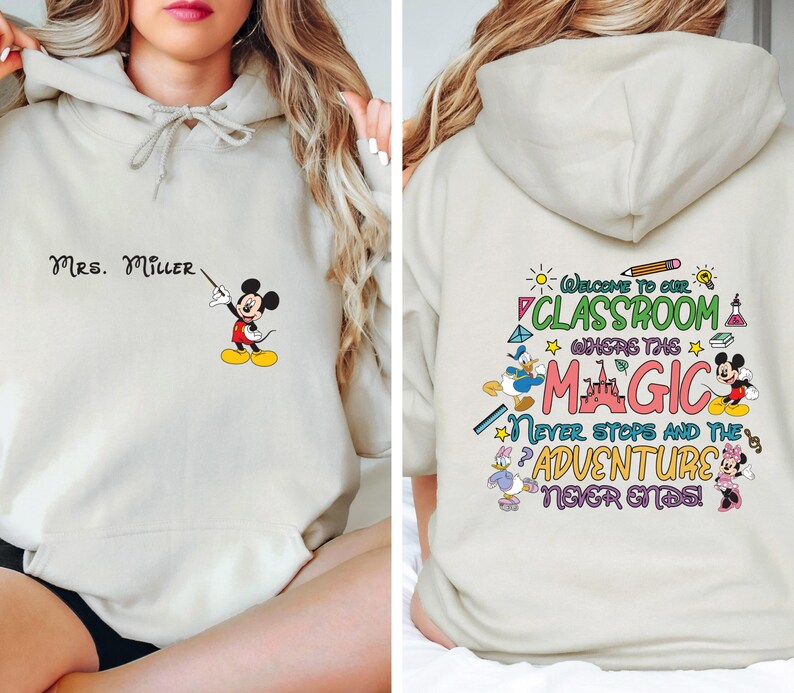 May include: A light beige hoodie with a Mickey Mouse illustration on the front and text that says "MRS. MILLER". The back of the hoodie has a colorful graphic with Mickey Mouse, Donald Duck, and Minnie Mouse characters and text that says "Welcome to our classroom where the magic never stops and the adventure never ends!"