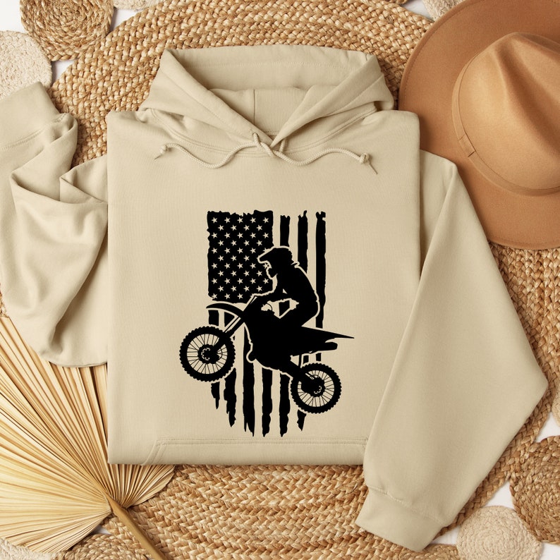 May include: A tan hoodie with a black silhouette of a motocross rider jumping over an American flag.