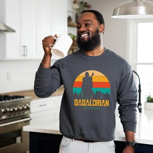 Puede incluir: Sudadera gris oscuro con un dise&ntilde;o gr&aacute;fico de una silueta contra un atardecer con el texto "DADALORIAN THIS IS THE WAY". Cuello redondo.