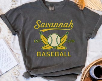 May include: Dark gray t-shirt with a yellow and white baseball graphic. The design includes the word "Savannah" above a baseball crossed with bananas, and the word "BASEBALL" below. The year "2016" is also included.