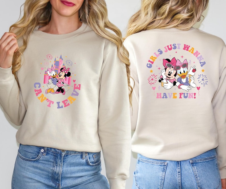 Puede incluir: Una sudadera de color crema con un gr&aacute;fico de Mickey Mouse y Daisy Duck frente a un castillo rosa. El texto "Can't Leave" est&aacute; escrito en un c&iacute;rculo alrededor del gr&aacute;fico. La parte posterior de la sudadera tiene un gr&aacute;fico de Mickey Mouse y Daisy Duck con el texto "Girls Just Wanna Have Fun!" en un c&iacute;rculo alrededor del gr&aacute;fico.