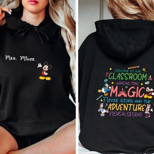 May include: Black hooded sweatshirt with a Mickey Mouse graphic on the front and text that says "Mrs. Miller". The back of the sweatshirt has a colorful graphic with the text "Welcome to our classroom where the magic never stops and the adventure never ends!"