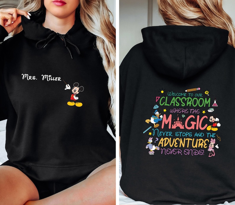 May include: Black hooded sweatshirt with a Mickey Mouse graphic on the front and text that says "Mrs. Miller". The back of the sweatshirt has a colorful graphic with the text "Welcome to our classroom where the magic never stops and the adventure never ends!"