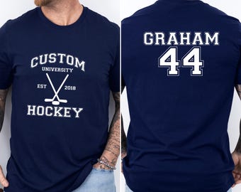 May include: A navy blue t-shirt with white text and a hockey stick graphic. The front of the shirt says "Custom University" with "EST 2018" and "Hockey" below. The back of the shirt says "Graham 44".
