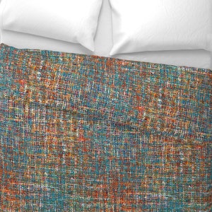 May include: A bed with two white pillows and a teal, orange, and blue patterned blanket. The blanket has a textured appearance with a woven design. The bed is covered in a white sheet.