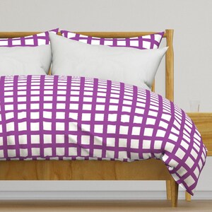 May include: A white and purple checkered duvet cover with a white and purple checkered pillowcase. The duvet cover is on a wooden bed frame.