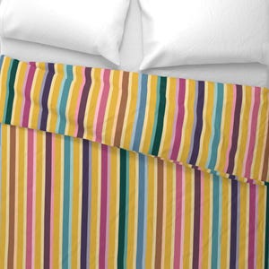 May include: A yellow, pink, blue, brown, and purple striped duvet cover with a white pillow on top.