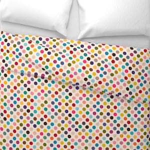 May include: A colorful polka dot pattern on a white background. The dots are in various colors, including red, blue, green, yellow, and purple. The pattern is on a bedspread with white pillows.
