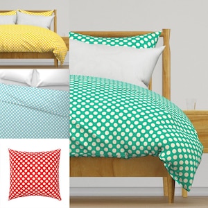 May include: A bed with a wooden frame is covered with a green polka dot duvet and white pillows. Additional bedding in yellow and light blue with white polka dots is also shown, along with a red pillow with white polka dots.