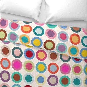May include: A duvet cover featuring a repeating pattern of multicolored circles on an off-white background. Each circle consists of a solid colored center surrounded by a contrasting ring, showcasing hues of red, blue, yellow, pink, and green.