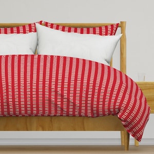 May include: Red and white striped duvet cover on a wooden bed frame. The duvet cover is made of a soft, comfortable fabric and features a simple, classic design.