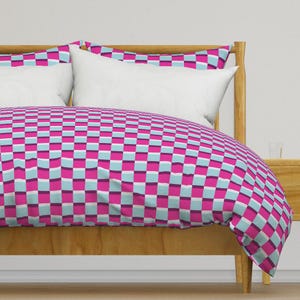 May include: A pink and blue checkered duvet cover with a white pillow on a wooden bed frame.