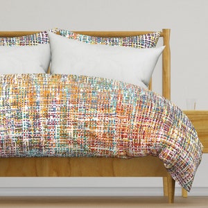 May include: A colorful duvet cover with a geometric pattern in shades of orange, red, blue, green, and white. The duvet cover is on a wooden bed frame.