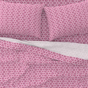 May include: Pink bedding set with a repeating pattern of pink and white circles. The set includes a flat sheet, fitted sheet, and two pillowcases.
