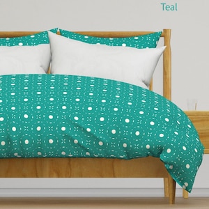 May include: Teal bedding set with a repeating pattern of white circles and crosses. The duvet cover and pillowcases are on a wooden bed frame. The word "Teal" is in the upper right corner.