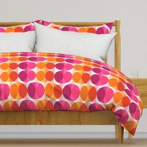 May include: A wooden bed frame with a white and pink patterned duvet cover. The duvet cover features a geometric pattern of overlapping circles in shades of orange, pink, and white.