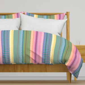 May include: A bed with a colorful striped duvet cover. The duvet cover has a pattern of vertical stripes in shades of pink, blue, green, and yellow. The bed has a wooden headboard and footboard.