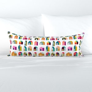 May include: A white lumbar pillow with a colorful geometric pattern of houses. The houses are in various shades of pink, red, yellow, blue, green, and brown.