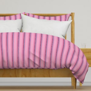 May include: Pink and purple striped duvet cover with a white pillow on a wooden bed frame.