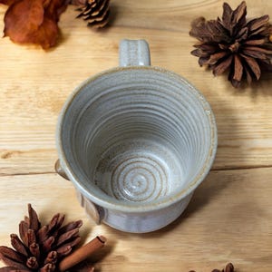 May include: A white ceramic mug with a brown glaze and a spiral design on the inside. The mug has a handle and a rounded bottom.