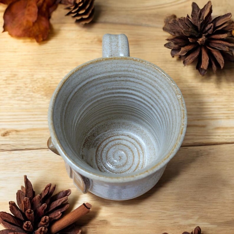 May include: A white ceramic mug with a brown glaze and a spiral design on the inside. The mug has a handle and a rounded bottom.