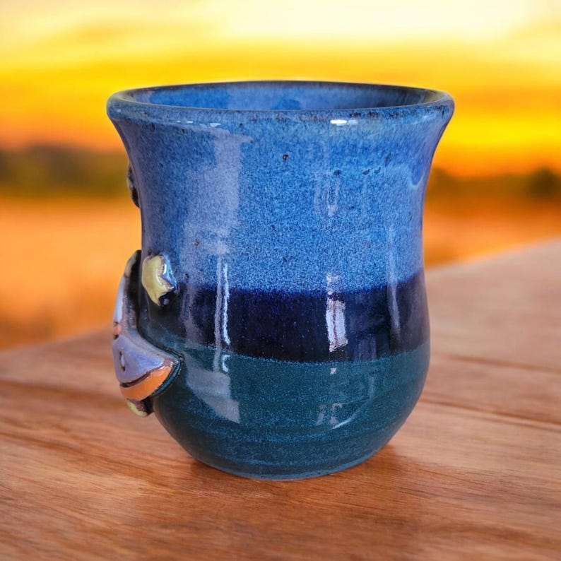K&ouml;nnte beinhalten: Eine blaue und gr&uuml;ne Keramiktasse mit einem 3D-Design eines Segelboots an der Seite. Die Tasse hat eine glasierte Oberfl&auml;che und ist handgefertigt.