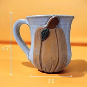 May include: A ceramic mug with a 3D pumpkin design. The mug is 4.5 inches tall and 3.5 inches wide. The pumpkin is painted in shades of brown, orange, and green.