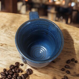 May include: A blue ceramic coffee mug with a textured glaze. The mug is empty and sitting on a wooden surface.